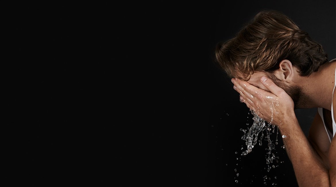 Ein junger Mann mit Drei-Tage-Bart spült sich sein Gesicht mit Wasser